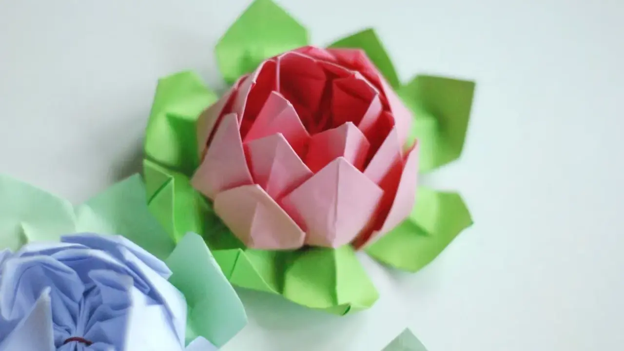 Różowy i niebieski kwiat origami prosty, otoczony zielonymi listkami.