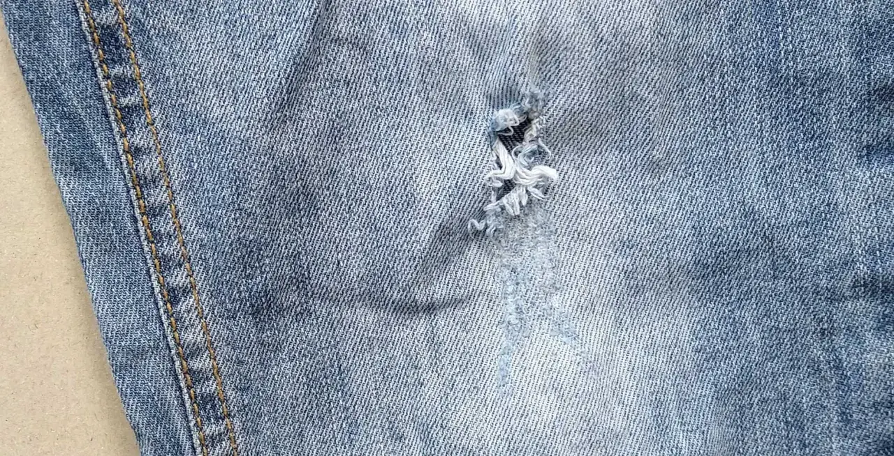Widoczna dziura w jeansach, z postrzępionymi nitkami, świadczy o intensywnym użytkowaniu.