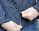Ręce zapinają suwak na wszyty zamek w granatowej, pikowanej kurtce.