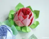 Różowy i niebieski kwiat origami prosty, otoczony zielonymi listkami.