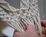 Ręce tworzą kwietnik makrama, pokazując, ile sznurka na kwietnik makrama potrzeba do wykonania skomplikowanych splotów.