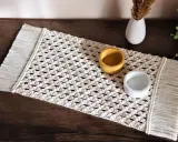 Bieżnik makrama z frędzlami, ozdobiony dwoma ceramicznymi naczyniami, dodaje rustykalnego uroku wnętrzu.
