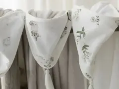 Trzy białe kocyki z motywami zwierząt i kwiatów, wykonane z delikatnego materiału, podobnego do batystu, z ozdobnymi chwostami.