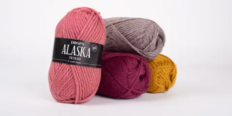 Kłębek różowej włóczki Drops Alaska z etykietą, obok innych kolorów. Idealna ilość włóczki na szalik.