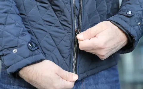 Ręce zapinają suwak na wszyty zamek w granatowej, pikowanej kurtce.