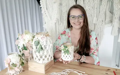 Uśmiechnięta kobieta prezentuje, jak zrobić lampion makrama. W tle widać gotowe ozdoby i materiały.