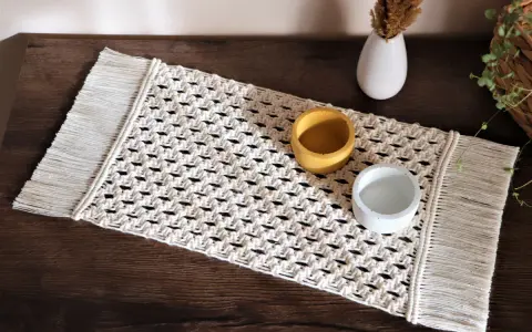Bieżnik makrama z frędzlami, ozdobiony dwoma ceramicznymi naczyniami, dodaje rustykalnego uroku wnętrzu.