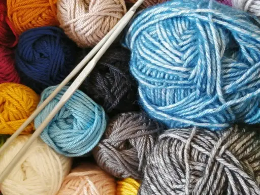 Kolorowe kłębki włóczki fantazyjnej i druty do robienia na drutach.