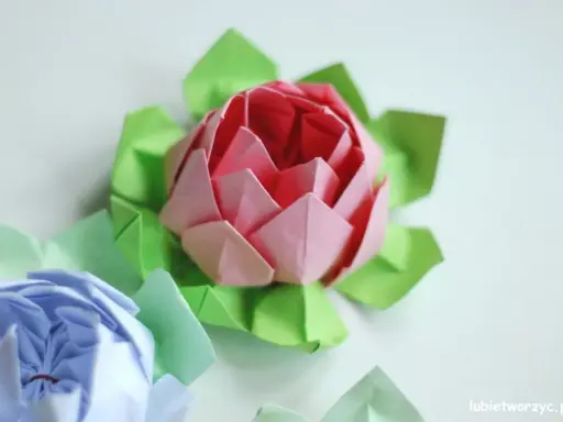 Różowy i niebieski kwiat origami prosty, otoczony zielonymi listkami.