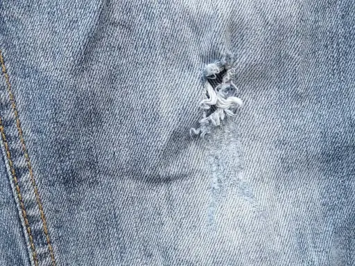 Widoczna dziura w jeansach, z postrzępionymi nitkami, świadczy o intensywnym użytkowaniu.