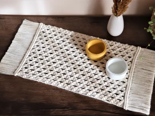 Bieżnik makrama z frędzlami, ozdobiony dwoma ceramicznymi naczyniami, dodaje rustykalnego uroku wnętrzu.