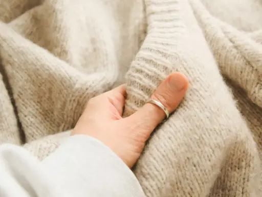 Dłoń dotyka miękkiego, beżowego swetra, ukazując różne rodzaje wełny owczej.