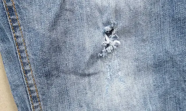 Widoczna dziura w jeansach, z postrzępionymi nitkami, świadczy o intensywnym użytkowaniu.